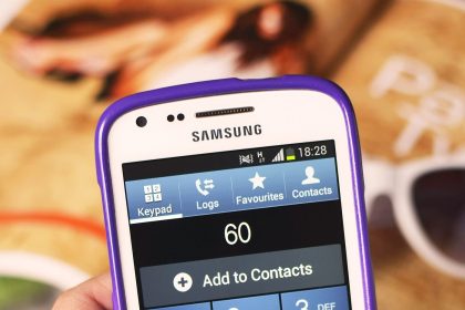 A shopper pays at a checkout by holding a smartphone near a payment terminal.